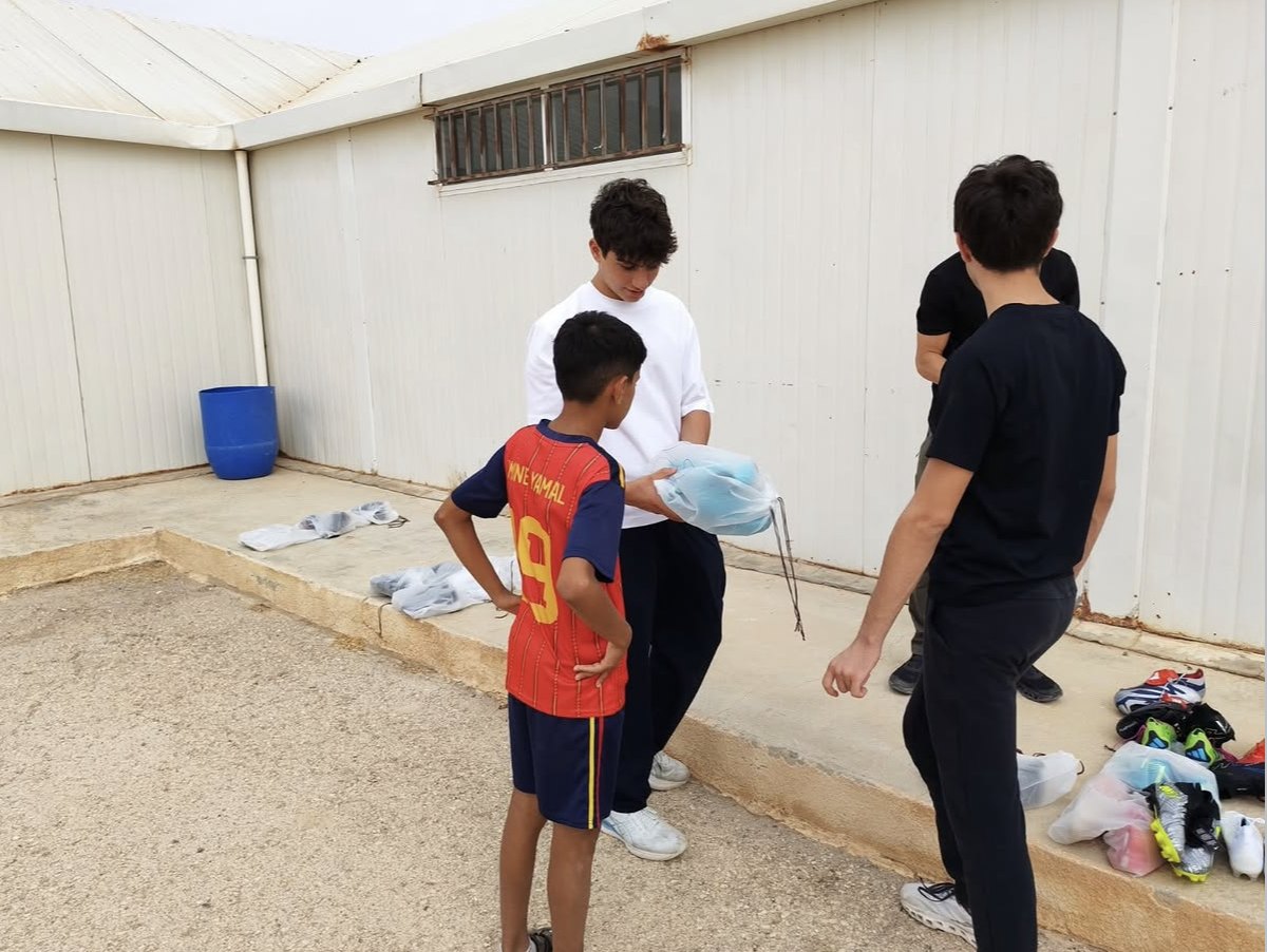 A Boots4Hope volunteer handing a bag of boots to a boy in a red number 9 shirt